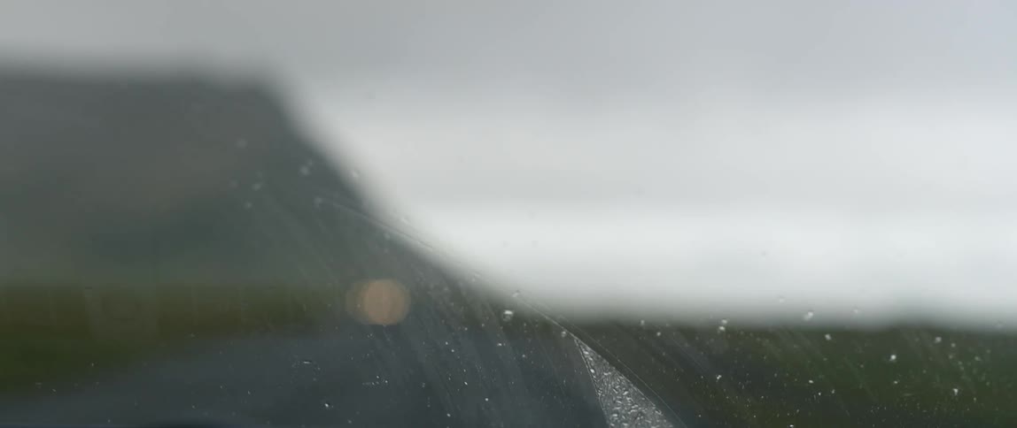 A car drives on a rural road in the rain