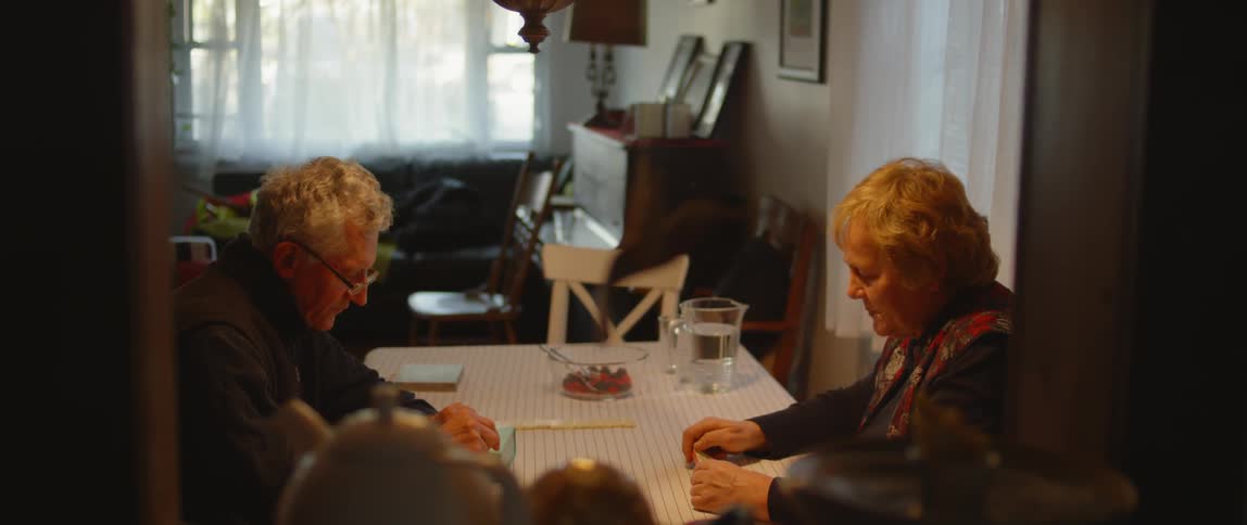 An elderly couple sit at a dining room table