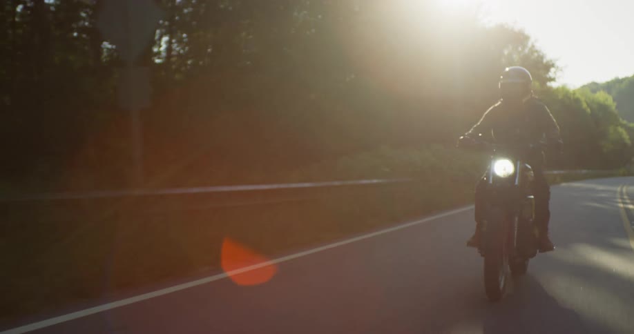 A person rides a motorcycle past trees on a sunny day