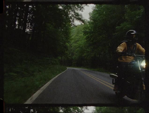A person rides a motorcycle on a rural road with headlight on