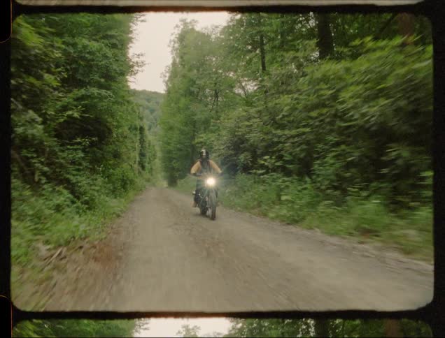 A man rides a motorcycle on a forest path