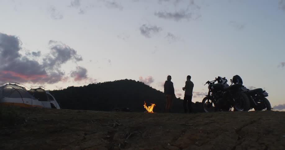 Two motorcyclists camp in mountains at sunset