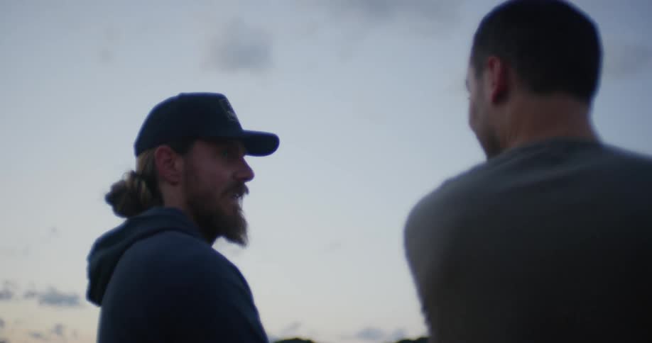 Two men are standing outside and talking at dusk