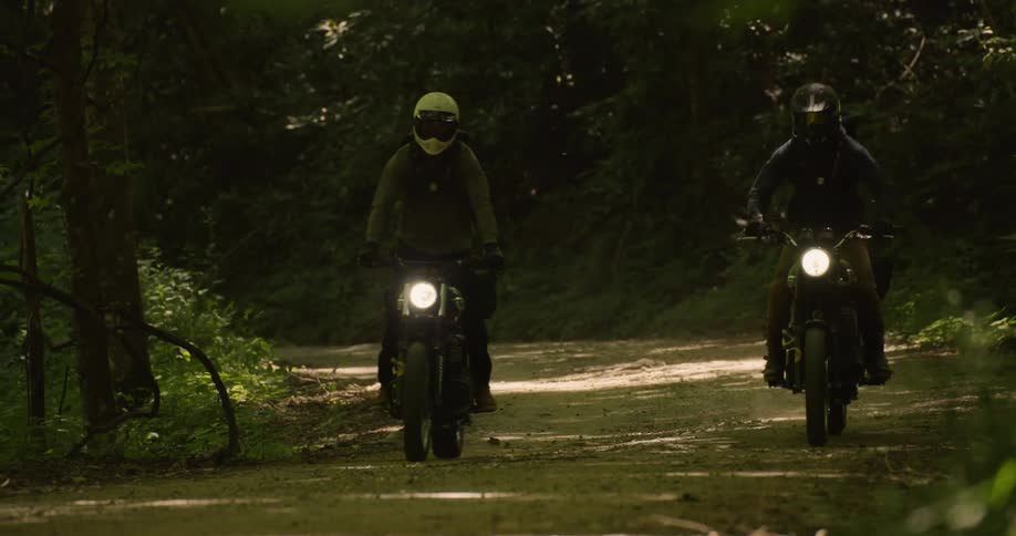 Two people are riding motorcycles on forest highway