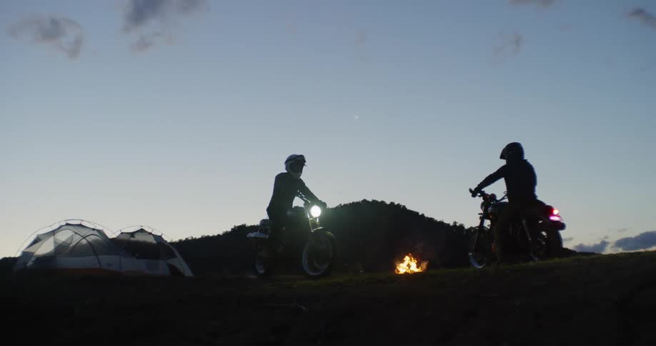 Two motorcyclists at a campground with a bonfire