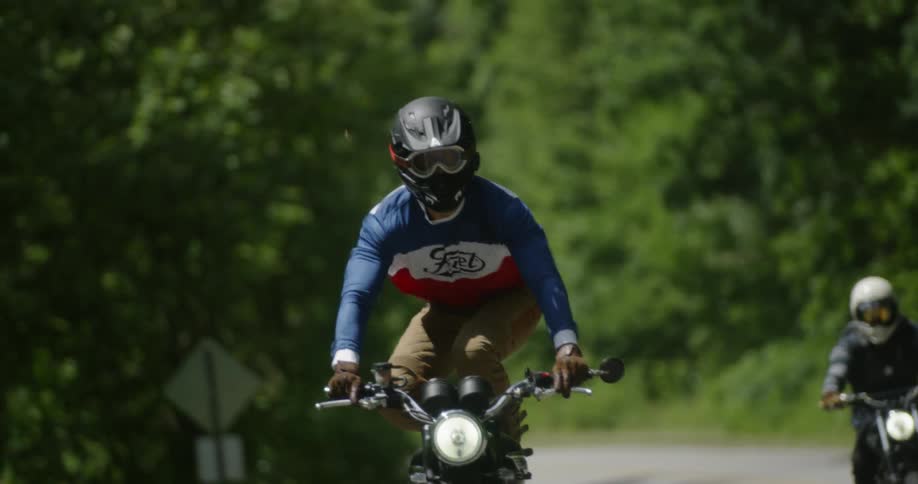 A motorcyclist stands on their bike on a rural road