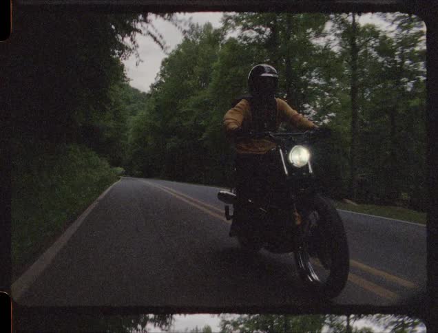 Man rides a motorcycle down a road near the trees