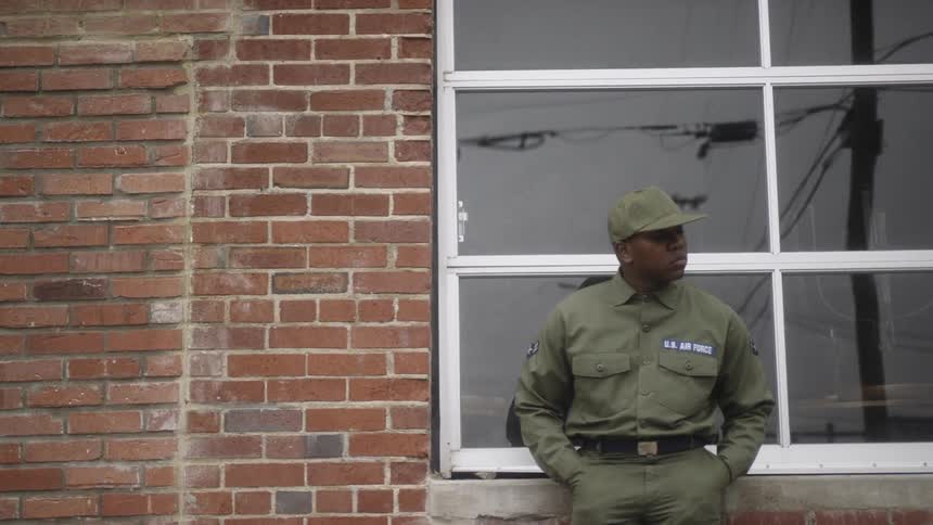 A service member leans against a brick building
