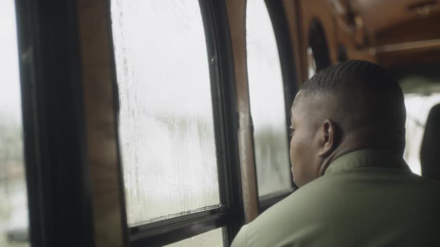 A man looks out a bus window while it rains