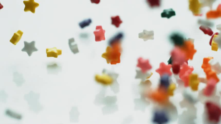 Colorful star sprinkles fall onto a white surface