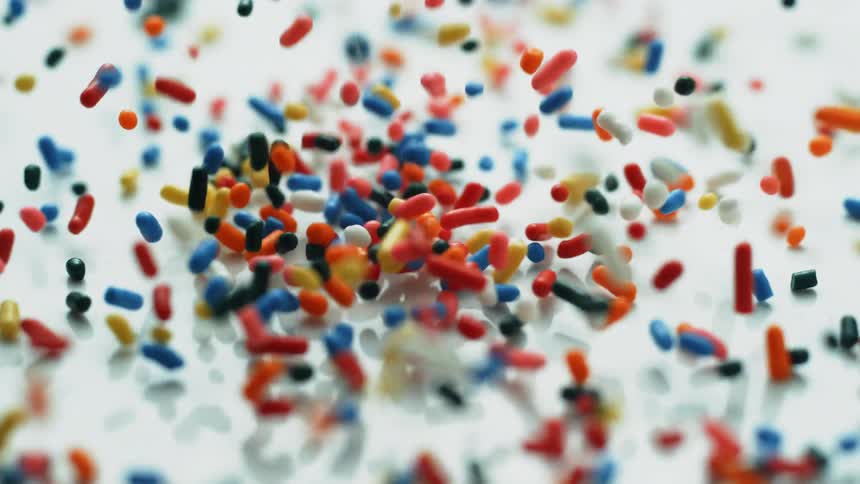 Colorful sprinkles fall onto a white surface