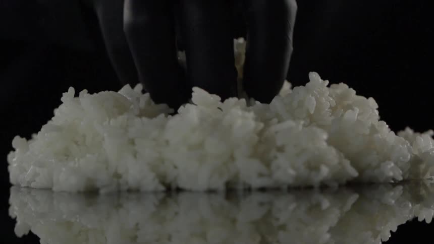 Gloved fingers pick up white rice from a pile