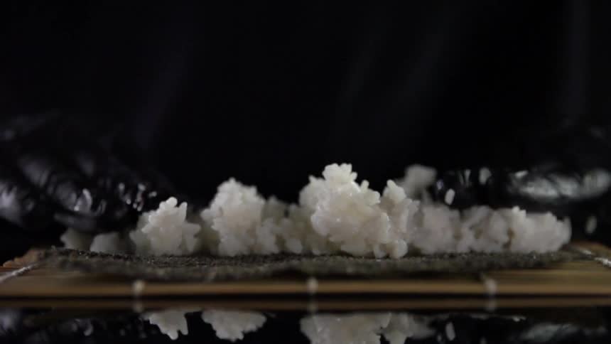 Black gloved hands press down on a mound of white rice