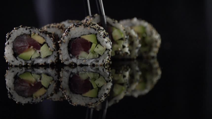 Pair of tongs picks up a piece of sushi