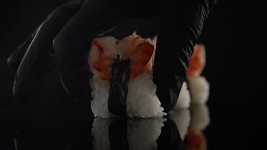 A gloved hand puts sushi on a table