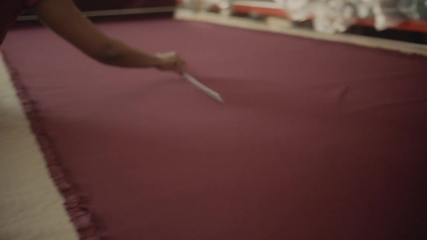 A woman smooths a large bolt of fabric on a worktable
