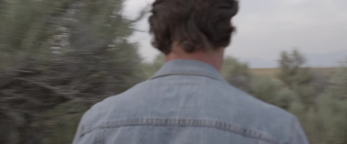 Man wearing a denim jacket walks near the trees