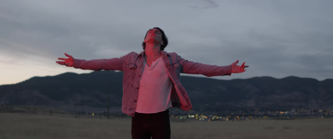 Man stands in a large field and raises his arms up
