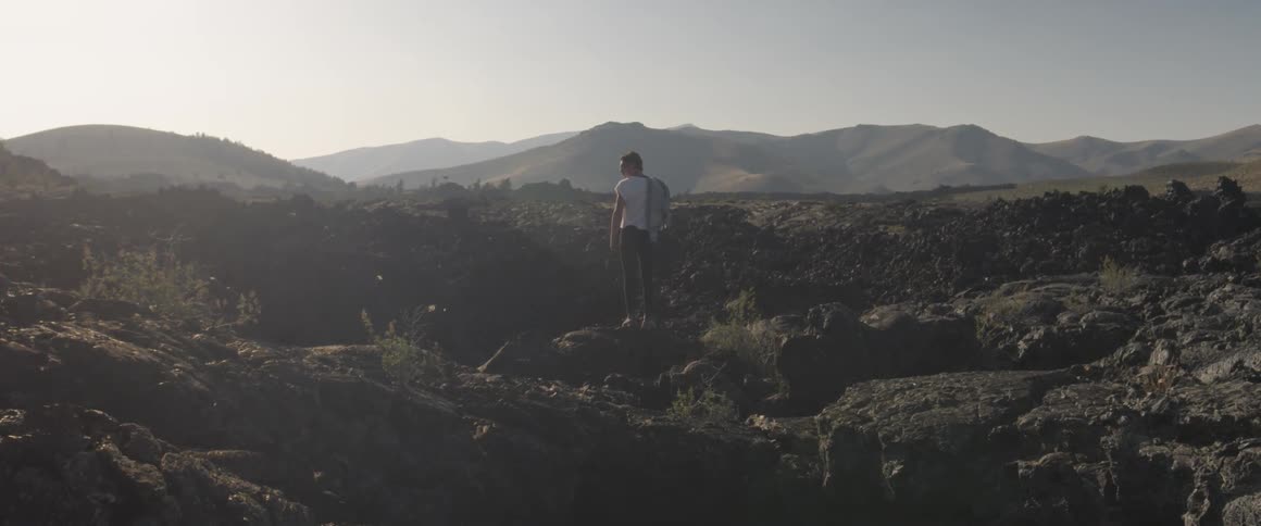 A man stands in a rural field at sunset