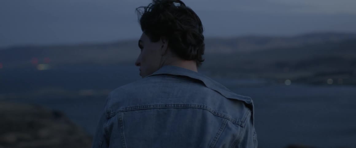 The wind blows a man's hair and clothing as he stands on a ridge
