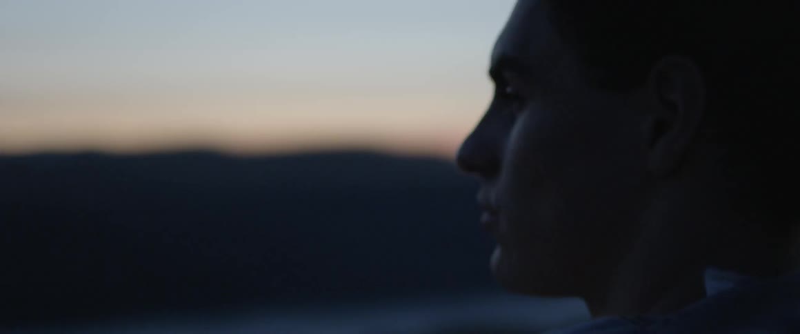 A man looks around outside at sunset