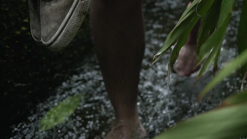 A man carries his shoes as he walks in the stream