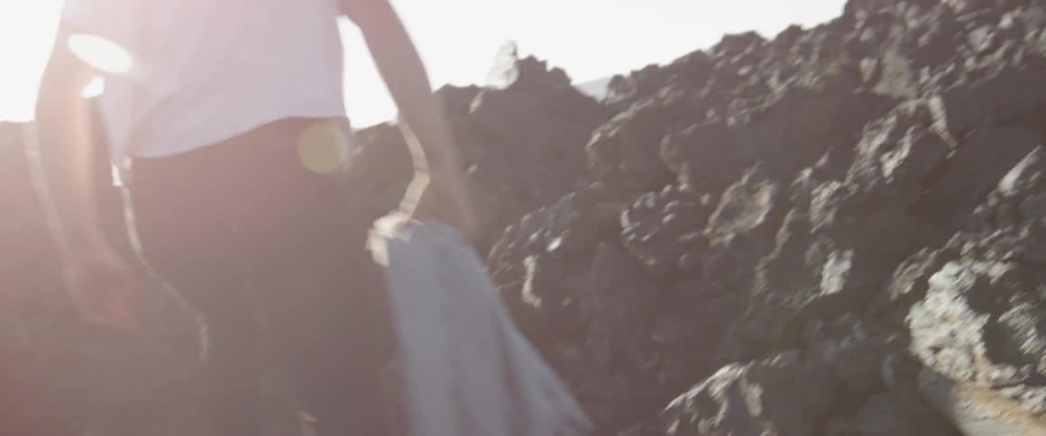 Man carries a coat and walks up a rocky hill on a sunny day