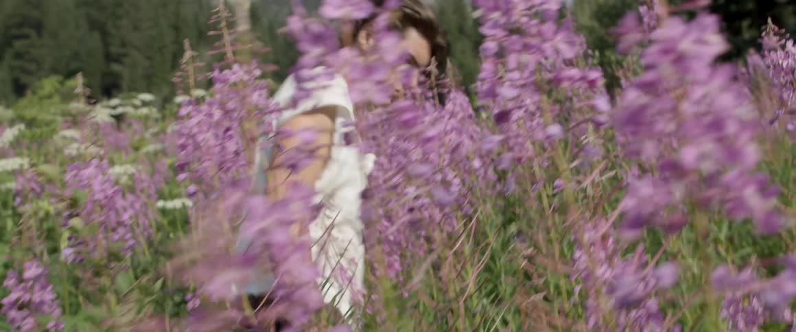 A man is touching the purple flowers in the long field