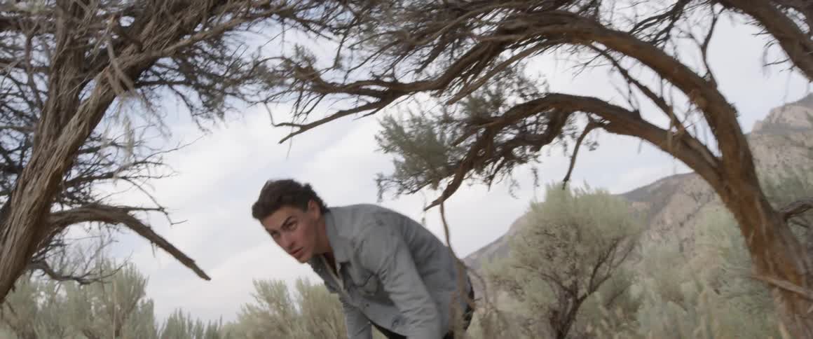 Man wearing a denim jacket walks and ducks under the low tree branches