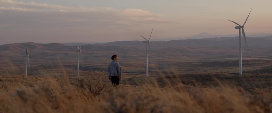 A man stands near the windmills on a windy day