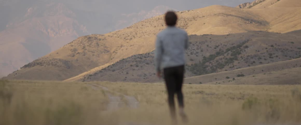 Man walks on a path towards hills