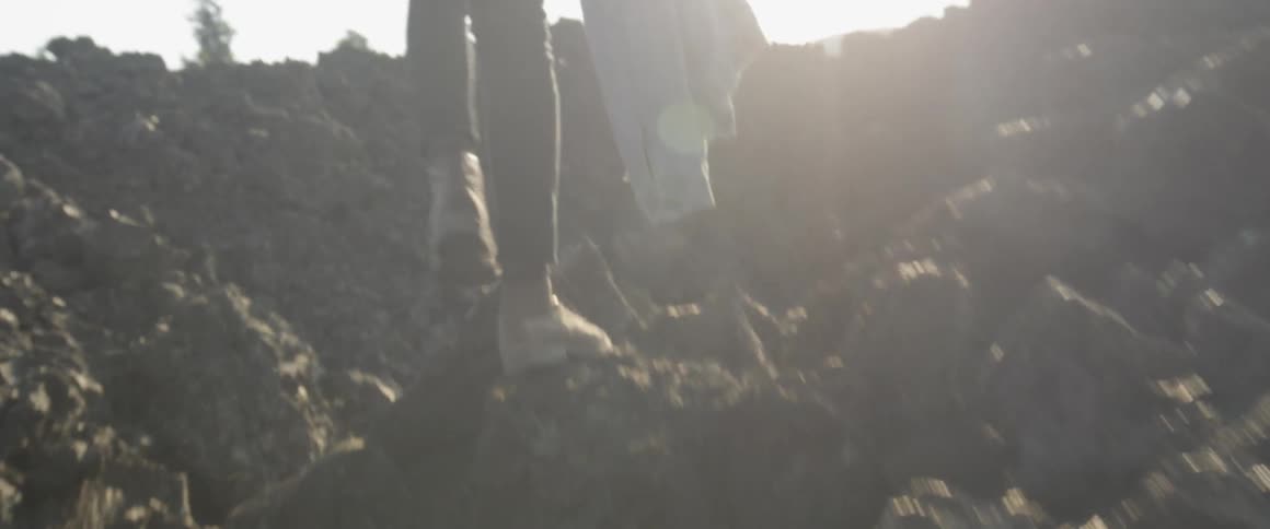 A man walks over jagged rocks while carrying his jacket