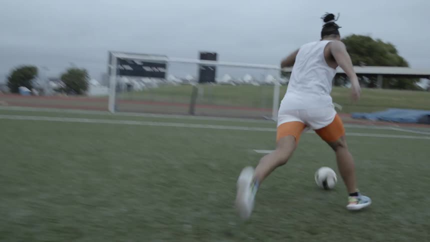 A soccer player is practicing shooting outside on a cloudy day