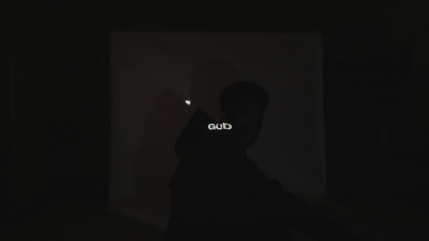 A man is sitting in front of a screen in a room as words are projected across him