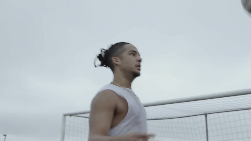 Man kicks a soccer ball in a field next to a goal post