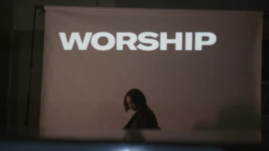 A woman sits in front of a projection screen with text