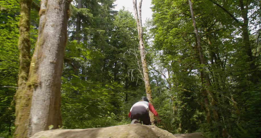 A man jumps off dirt ramps on a forest path