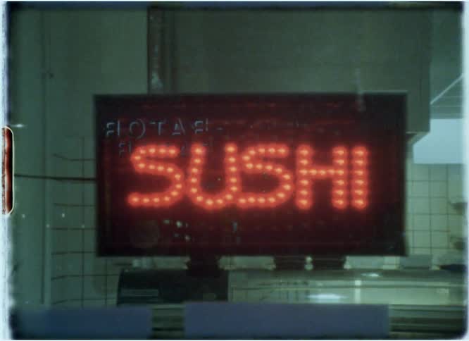 A sign for sushi illuminates in the storefront window