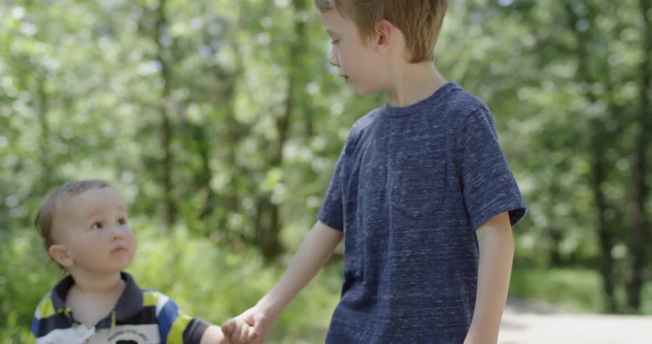 A young boy walks a toddler through the woods