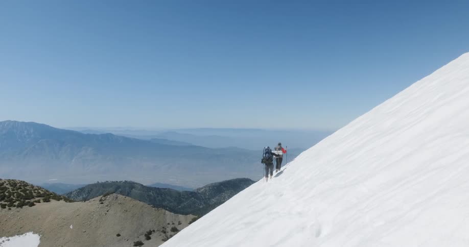 Two hikers trek on the side of the snowy mountain