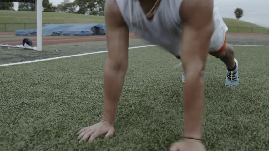 A man does push ups outside on an athletic field