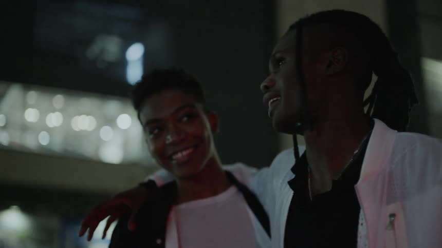 A man and woman are talking outside at night in a city