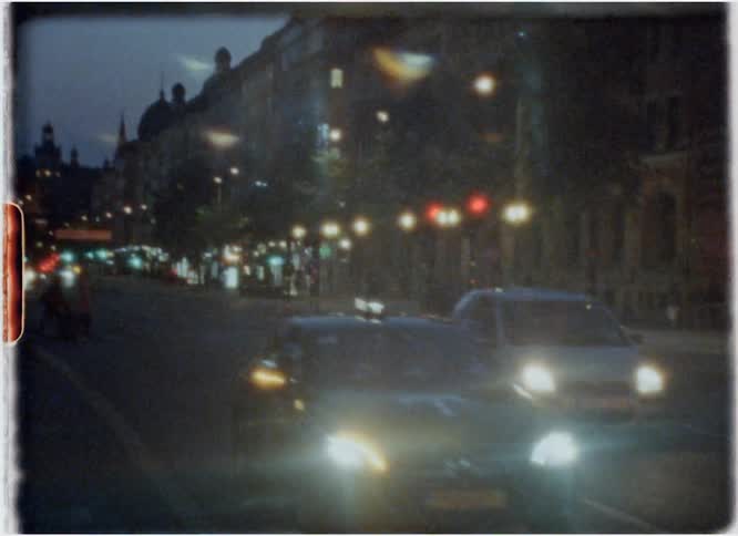 Cars are driving down a city street at dusk