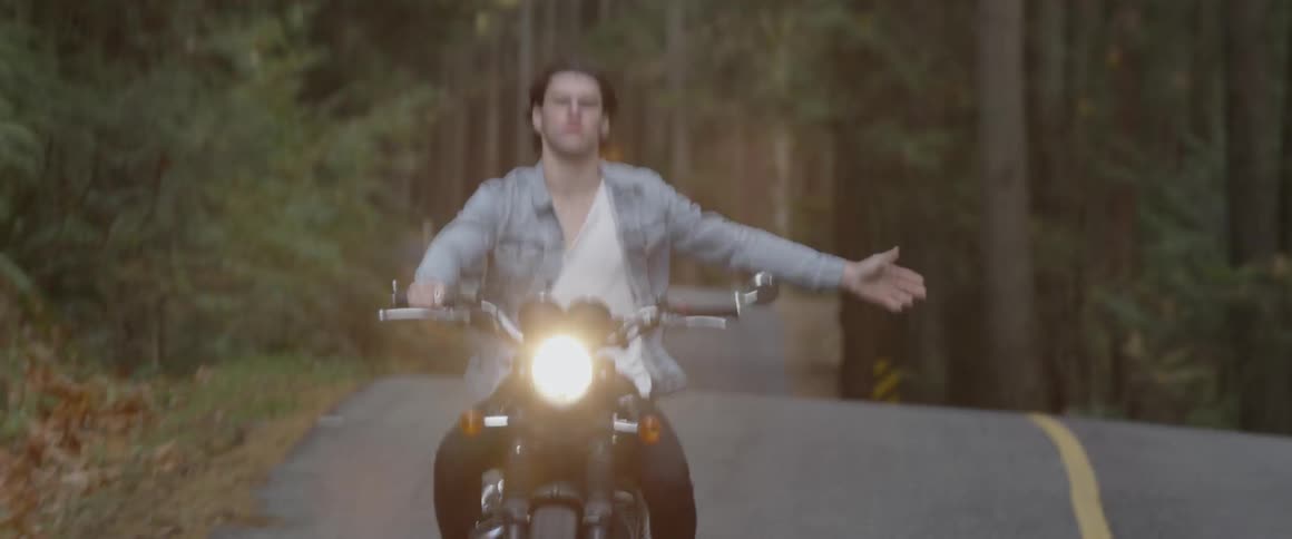 A man rides a motorcycle and outstretches his arm