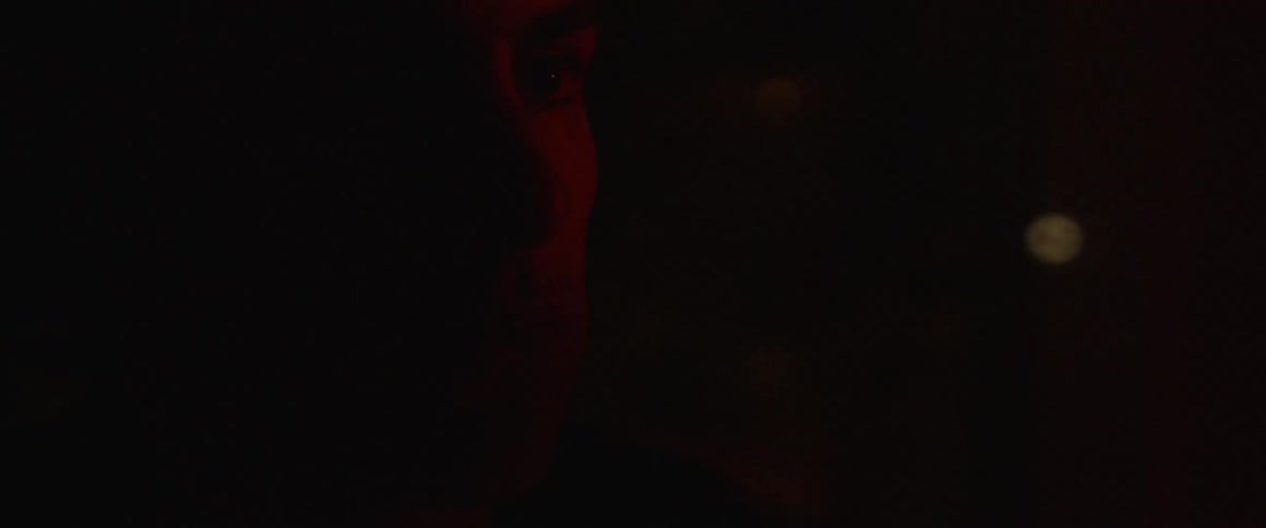 A red light shines on a man's face and he bows his head