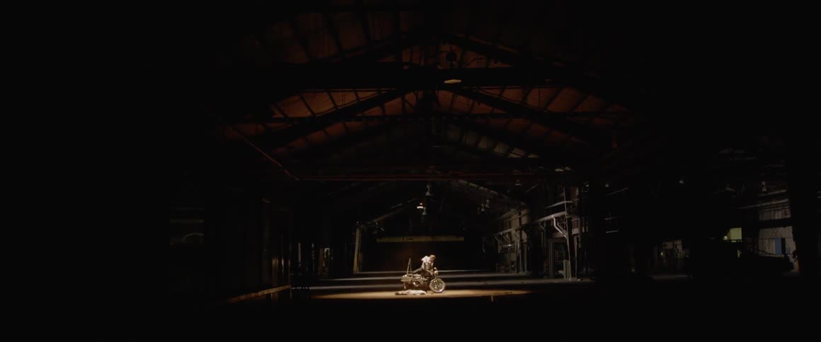 Person takes a white cloth off a bike in a large dark room