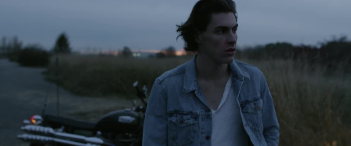 A man walks past his parked motorcycle on a rural road