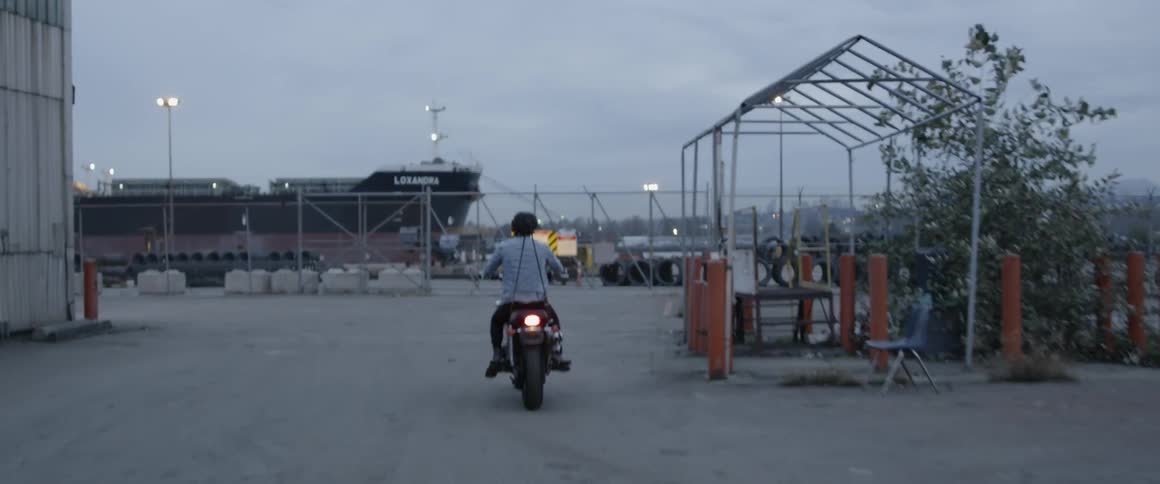 Man rides a motorcycle towards a chain link fence