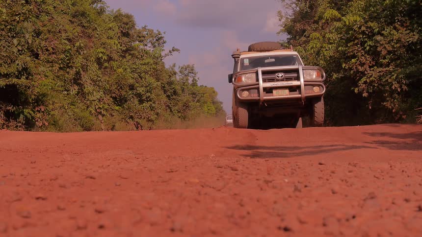 Vehicles travel down a dirt road on a sunny day