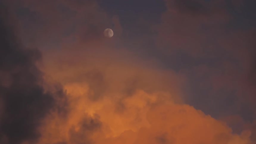 The moon is shown at dusk above moving clouds